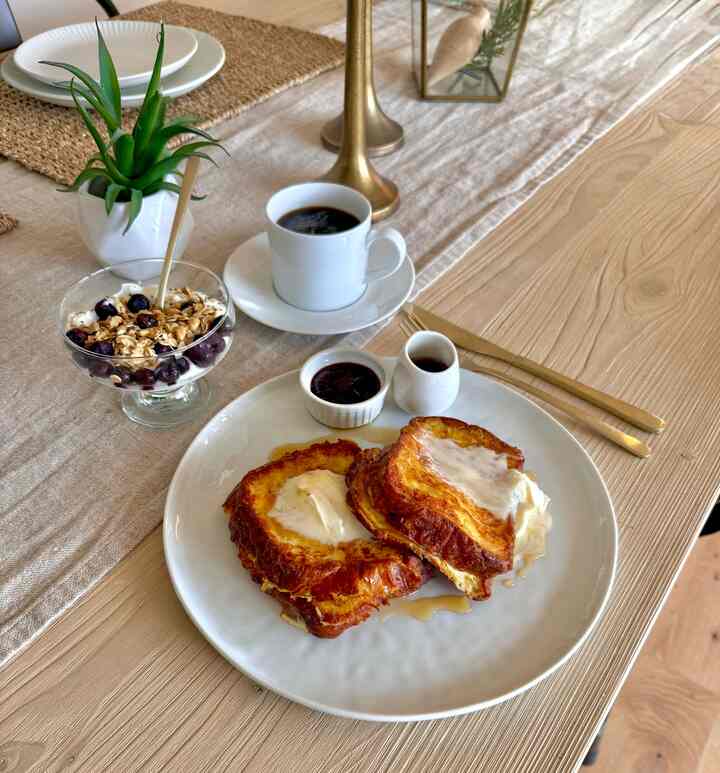 Natural wood tone dining table featuring croissant French toast and coffee, creating a warm brunch atmosphere