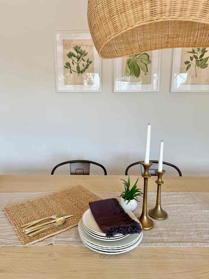Natural toned dining room featuring wooden dining table, gold candle holders, and dark napkins creating cozy ambiance
