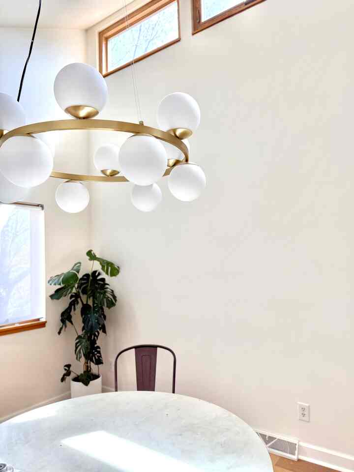 Modern dining room with white walls and ceiling, featuring a marble dining table and a gold chandelier, bright space with a plant on the left