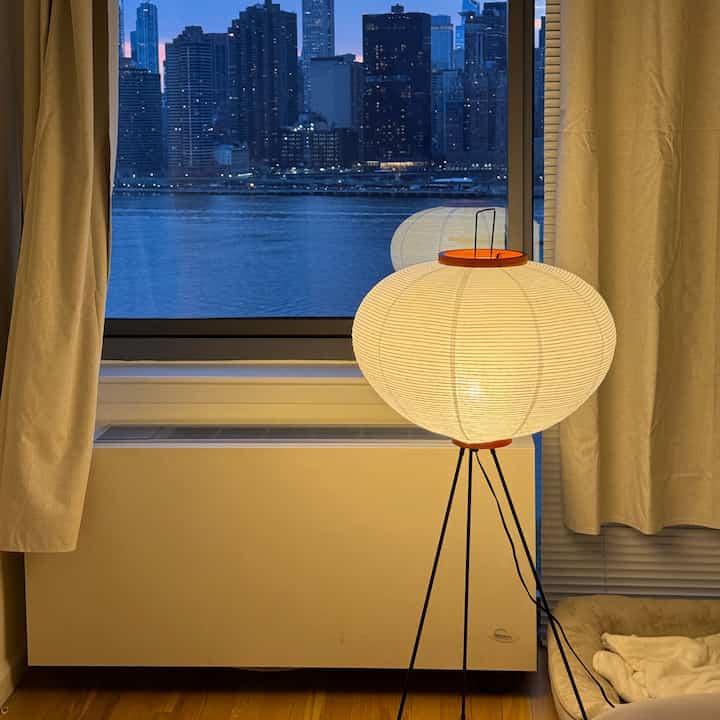 Natural-toned curtains and pet bed in a cozy mid-century modern bedroom with city skyline visible through the window