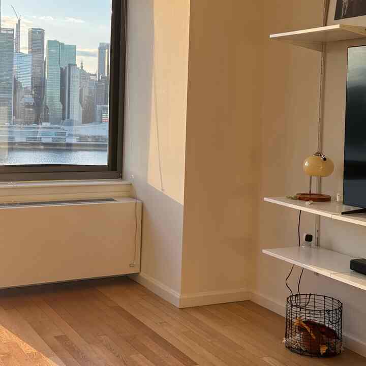 Cozy small space with white and wood tones featuring wall-mounted desk and shelves near window, and a wire basket on wooden floor
