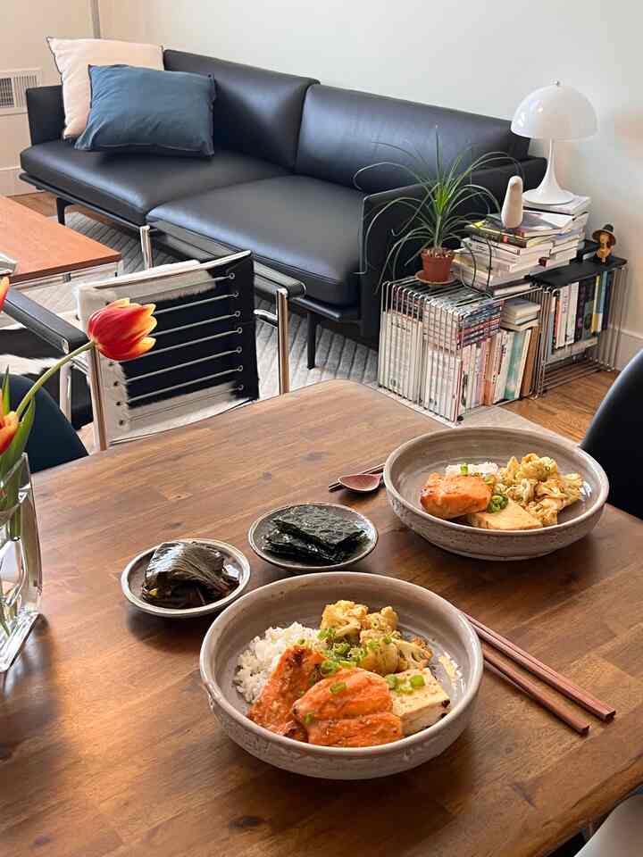 Natural wood tone dining room with modern black furniture, cozy space featuring simple Korean dishes on the dining table
