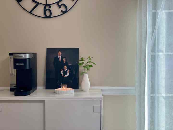 A white and beige toned living room featuring a coffee maker, sheer curtains, lit candle, and decorative vase in a minimalist setting