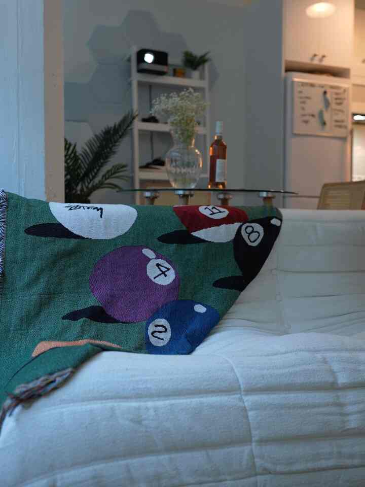 White and green toned living room featuring a white sofa with billiards-themed throw, presenting a simple and minimal atmosphere