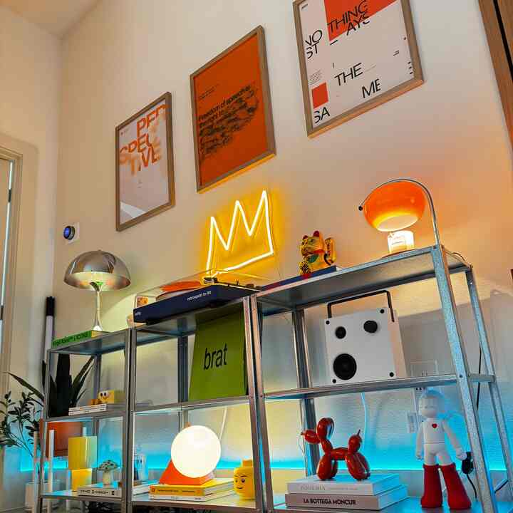 Living room with orange and gold tones featuring various lamps and decorative objects arranged on metal shelving, creating a lively atmosphere