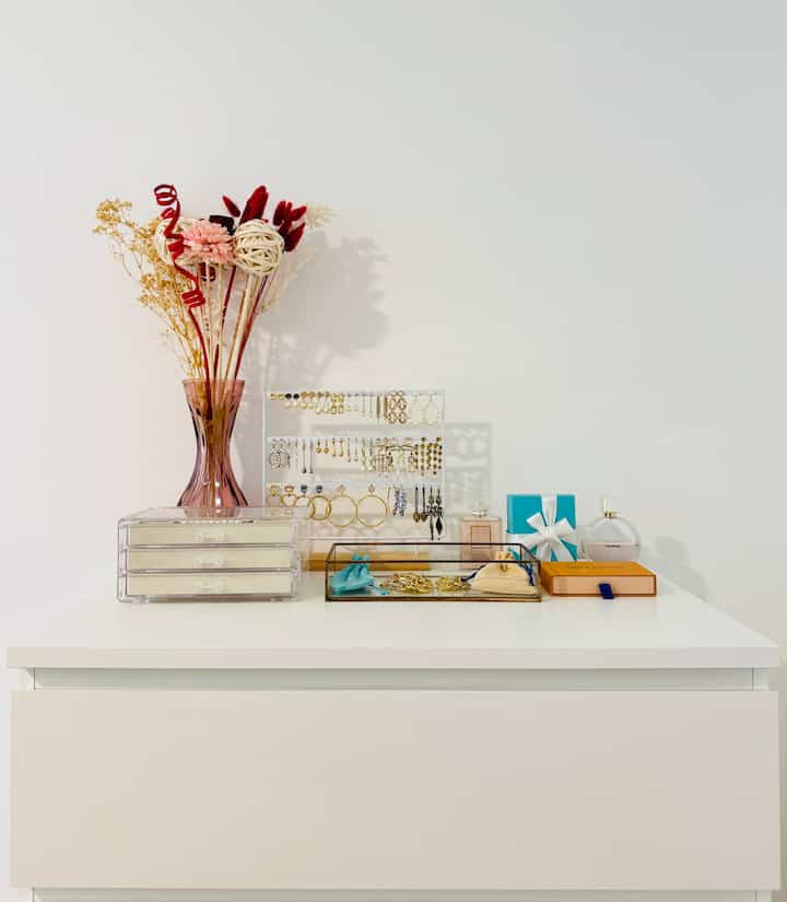 Minimal white chest of drawers featuring transparent acrylic jewelry organizer and decorative vase with a clean, simple atmosphere