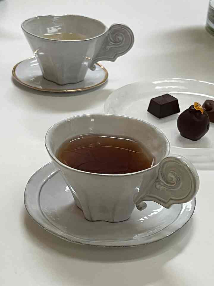 A white table featuring two art deco style teacups and chocolates for a cozy teatime setup