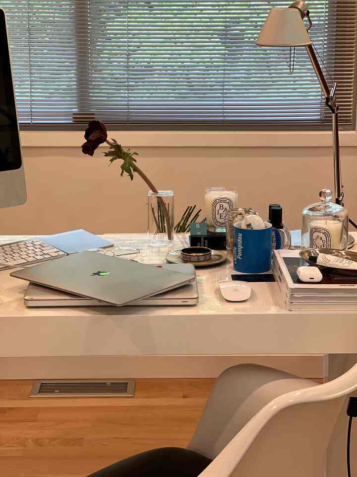 White-toned home office space featuring modern desk, office chair, candles, and desk lamp with cozy ambiance