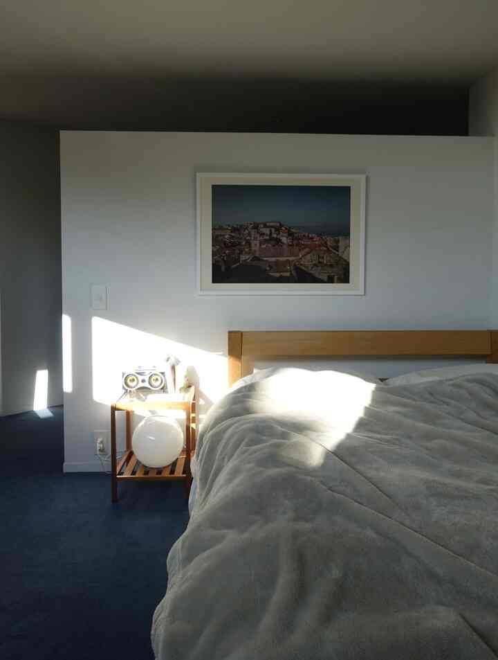 白い壁と青いカーペットの寝室、木製のベッドとナイトテーブル、ポスターが配置された清潔感のあるシンプルなインテリア