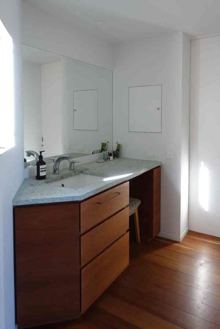 白い壁とナチュラルな木製キャビネットが配置されたバスルームの洗面スペース、明るく清潔感のある雰囲気