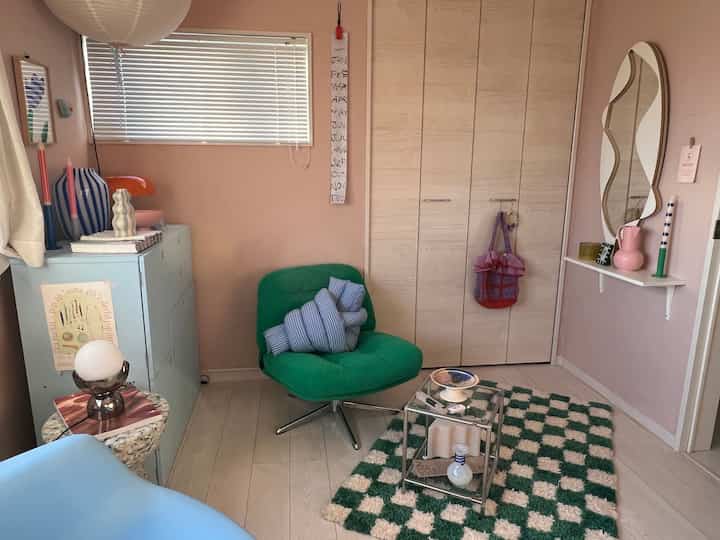 ピンク色の壁と白い床を持つリビングルーム、グリーンのアームチェアとチェック柄のラグが配置された雰囲気のあるレトロなインテリア