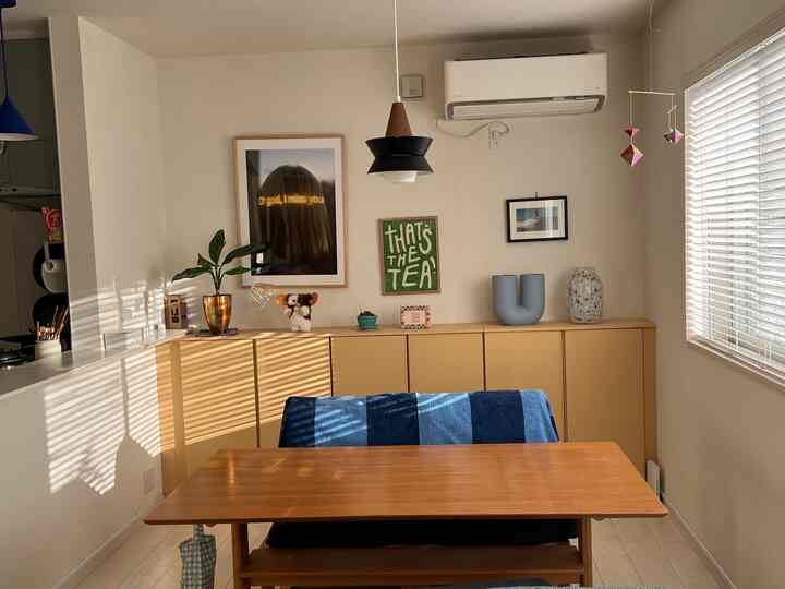 ベージュと木目調のダイニング、壁面に収納キャビネットが置かれ、小物と額装が配された温かみのあるインテリア