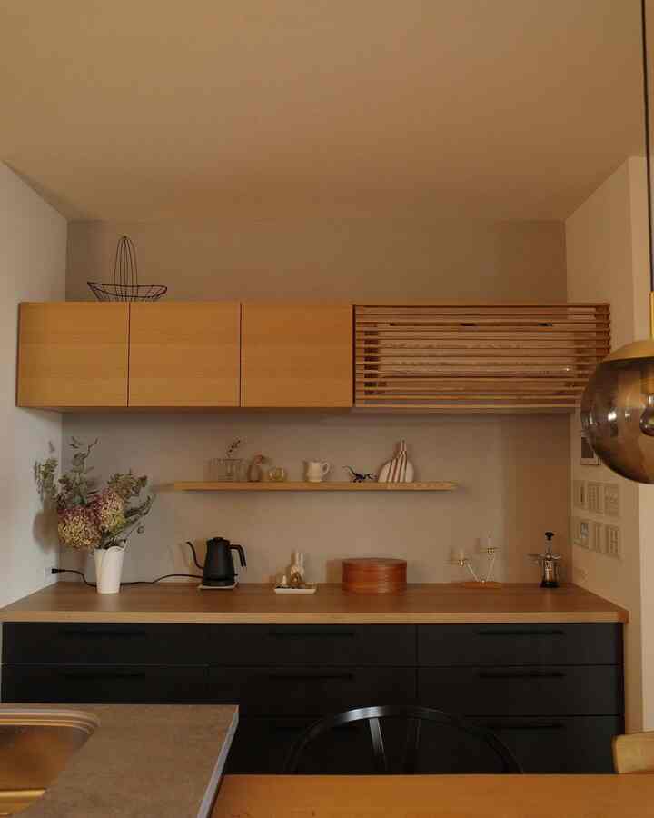 ナチュラルな木目調とモダンなデザインのキッチン、木製キャビネットとオープンシェルフ、電気ケトルが配置された清潔感のある空間