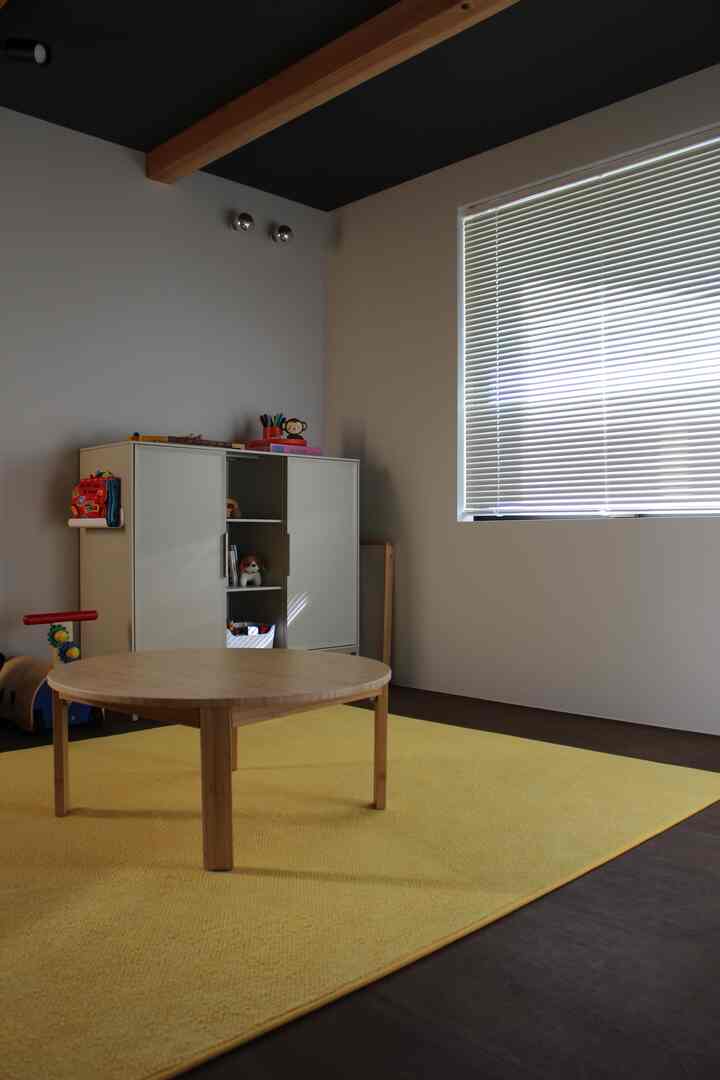 黄色いラグと木製のコーヒーテーブルが配置された子供部屋、白い壁とブラインドのある清潔感のあるインテリア
