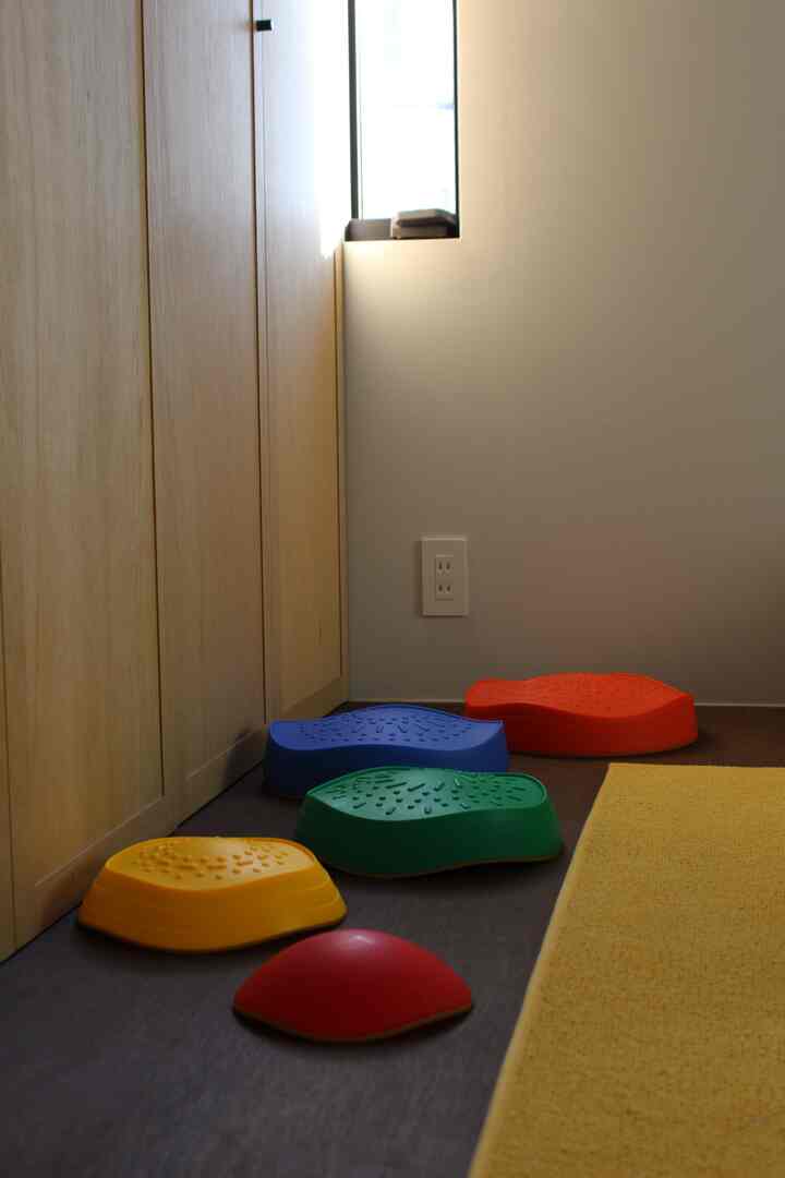 明るい黄色のラグとカラフルなバランスストーンが配置された子供部屋、自然な木目の家具と調和した雰囲気のあるインテリア