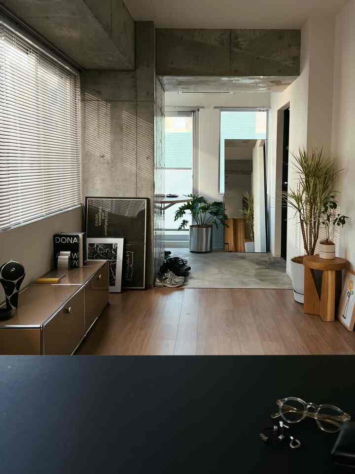 グレーのコンクリート壁と木目調の床が印象的な玄関とサイドボード、植物が配置されたモダンな雰囲気のインテリア