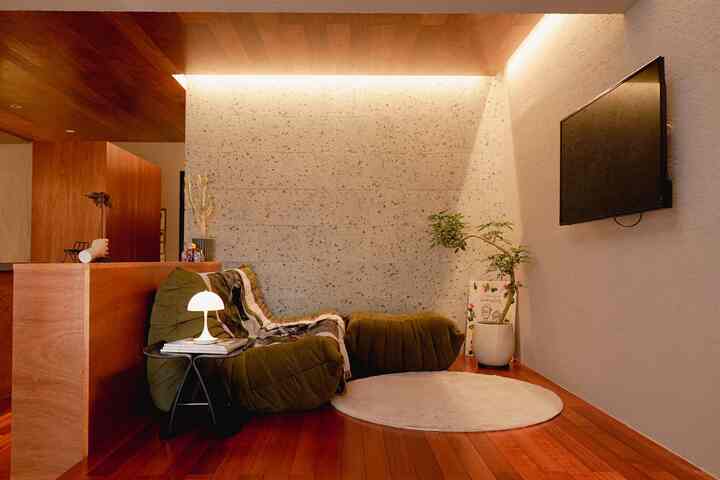 温かみのある木目調とナチュラルモダンの玄関兼リビングエリア、オリーブ色の2人掛けソファとフロアランプが配置された印象的な空間