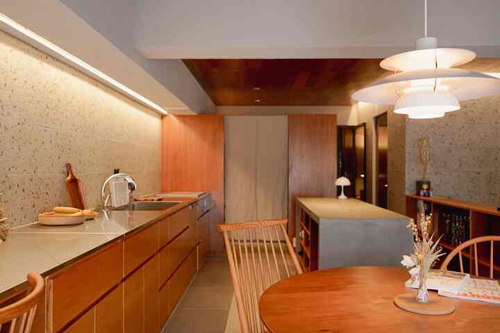 温かみのあるウッドトーンとベージュの壁が調和するキッチンとダイニングスペース、モダンなペンダントライトが印象的な空間