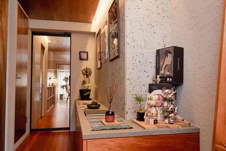 ナチュラルな木目調とベージュの壁紙の玄関、飾り物と植物が置かれた収納キャビネットが配された雰囲気のある空間