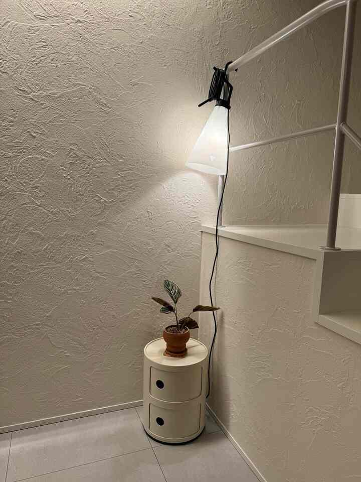 アイボリーの質感の壁とライトグレーの床、コーナーに配置された白い丸い収納棚とやわらかな間接照明がある落ち着いた空間