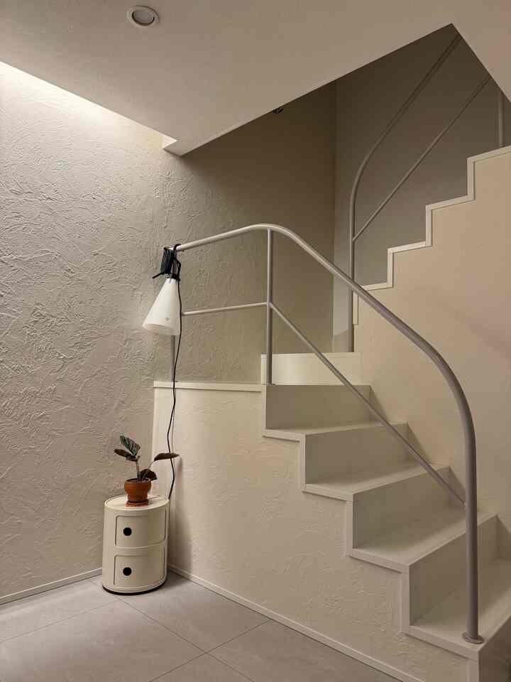 柔らかなベージュと白を基調とした階段空間、コーナー収納と照明が配置されたナチュラルモダンなインテリア