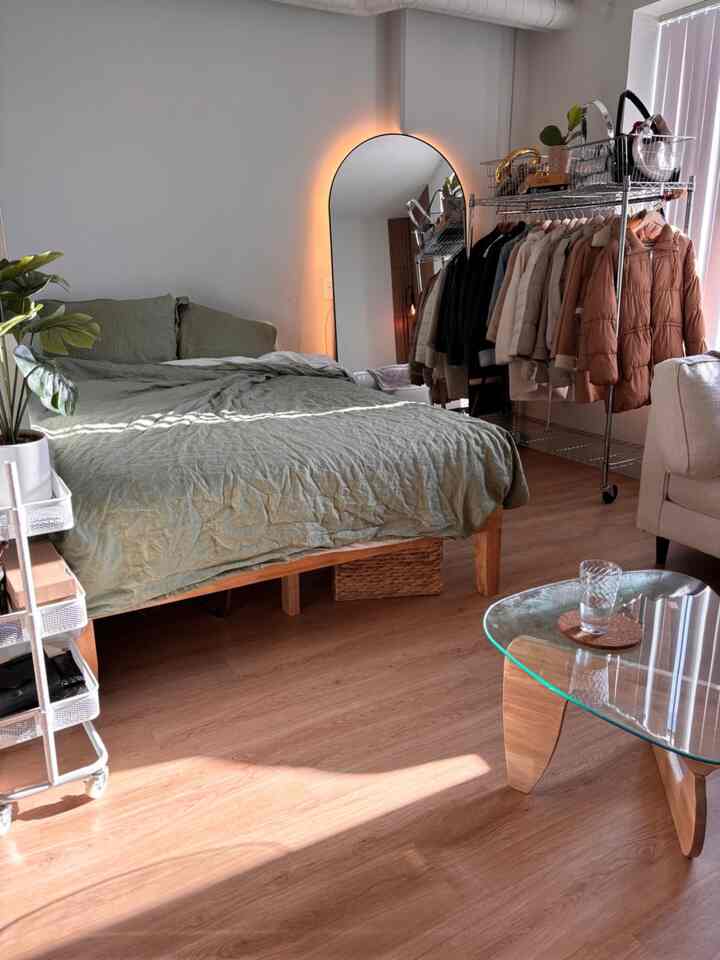 Natural wood-toned studio bedroom with green bedding, featuring a simple and cozy Japandi style space