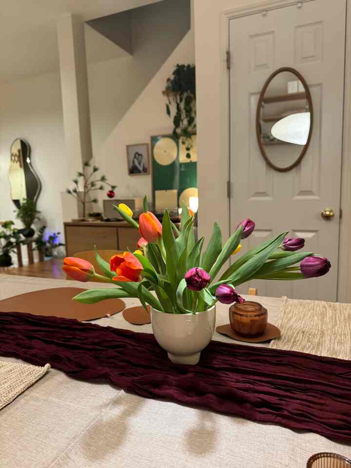 Beige-toned dining room featuring a central table with a burgundy runner and a vase of colorful tulips, creating a cozy atmosphere