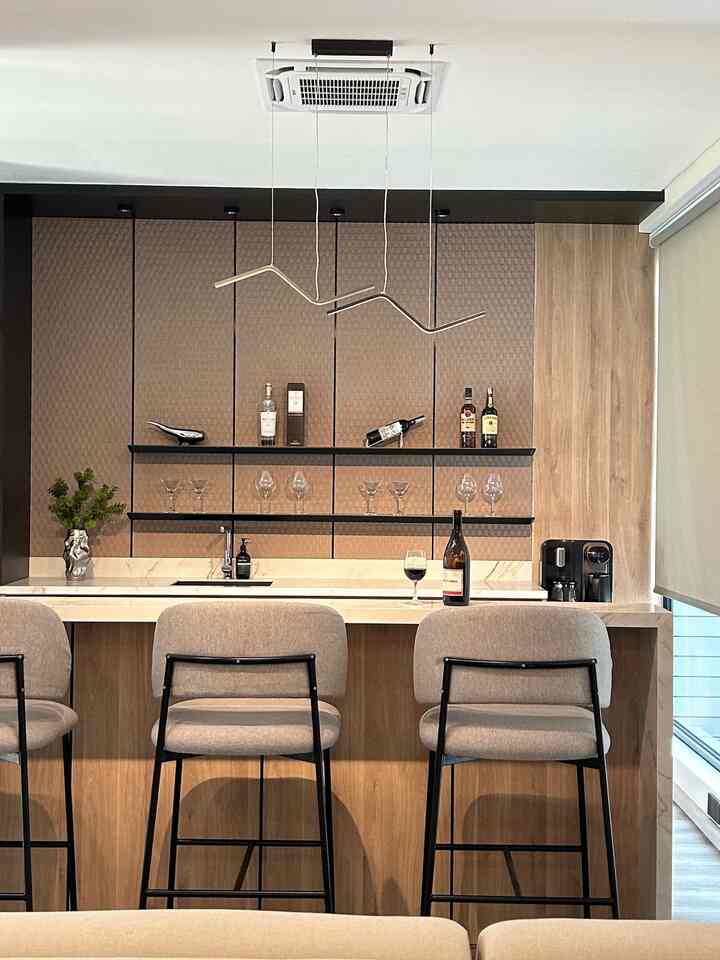 Ruangan ini memiliki desain modern dan elegan, dengan konsep minibar yang nyaman untuk bersantai. Area bar dilengkapi dengan countertop marmer putih yang memberikan kesan mewah, sementara latar belakang dengan panel berpola geometris menambahkan sentuhan artistik. Rak gantung yang rapi menampilkan koleksi botol minuman dan gelas kaca, menciptakan suasana yang sophisticated.

Kursi bar dengan sandaran empuk dan rangka hitam memberikan kenyamanan sekaligus memperkuat tampilan modern. Pencahayaan gantung dengan desain unik memberikan aksen yang menarik sekaligus menghadirkan pencahayaan yang hangat. Perpaduan material kayu pada kabinet dan sentuhan marmer menciptakan harmoni yang estetis. Ruangan ini cocok untuk tempat bersantai atau menghibur tamu dengan gaya yang berkelas. 
#minibar #homekitchen #backsplash #lampudapur #lampubar #filterair #waterfilter #wineglass #botolestetik 