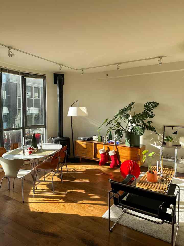 White and wood-toned living and dining room featuring mid-century modern furniture with red holiday decorations in a warm setting