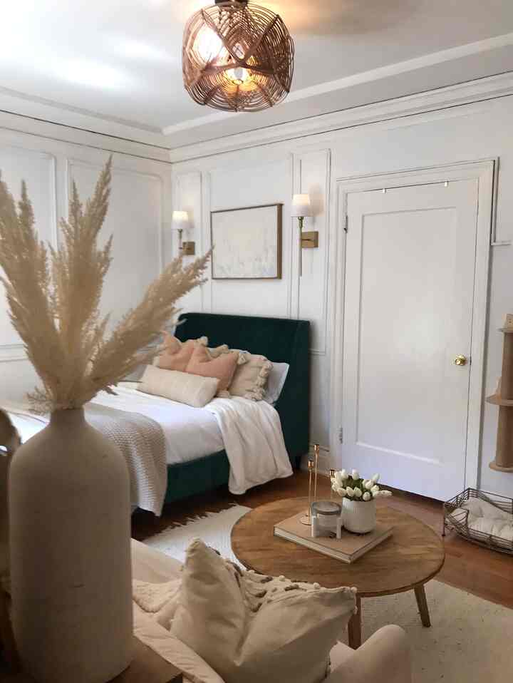 Natural modern studio apartment with white and brown tones featuring a green bed and round wooden coffee table, creating a cozy bedroom-living hybrid space