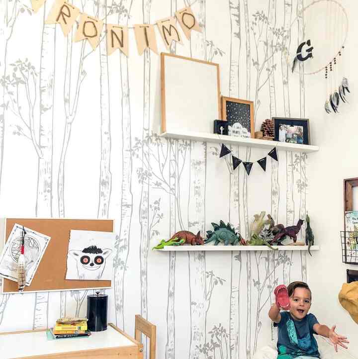 Natural kids' room with white tree-patterned walls, a child’s desk, and shelves displaying dinosaur toys creating a playful atmosphere