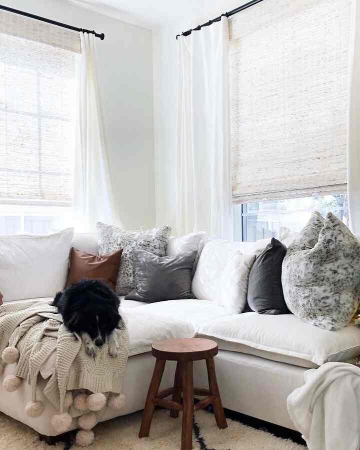 A white and beige toned living room featuring a large sectional sofa with cushions and blankets, and a black dog resting comfortably