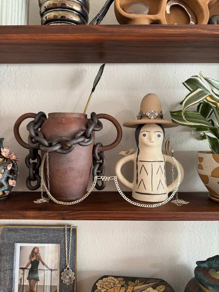A warm-toned shelf with natural brown and ivory hues featuring Bohemian-style ceramic chain vase and protector doll decor
