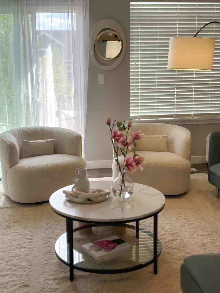 A white and beige toned living room featuring a round coffee table and two armchairs, creating a cozy natural atmosphere