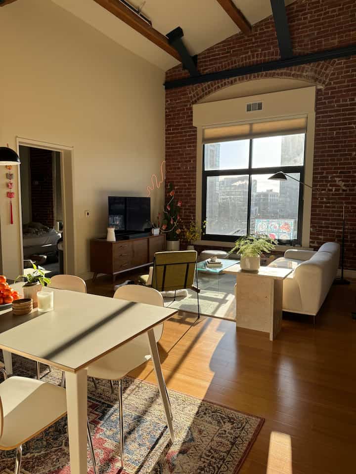 Natural brown and white toned living and dining room for four, featuring a large window and mid-century modern furniture with warm atmosphere