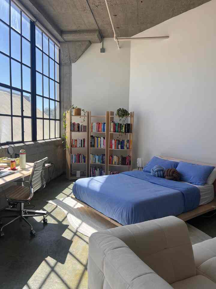Natural-tone loft bedroom featuring a blue-bedded bed and bookshelves with a bright, cozy atmosphere