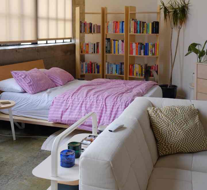 Cozy bedroom with pink bedding and natural wood bookshelf, featuring a white sofa in foreground