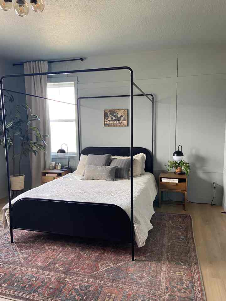 A cozy bedroom in soft gray and beige tones featuring a black metal frame bed and wooden nightstands centrally arranged