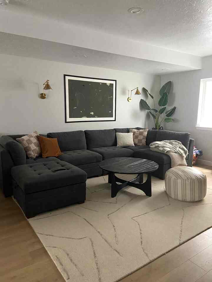Natural toned living room featuring a large dark gray sectional sofa, cream rug, and round coffee table with a cozy atmosphere