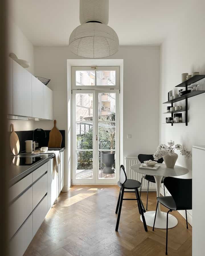 Bright white-toned kitchen featuring modern dining table and chairs with abundant natural light creating a cozy atmosphere