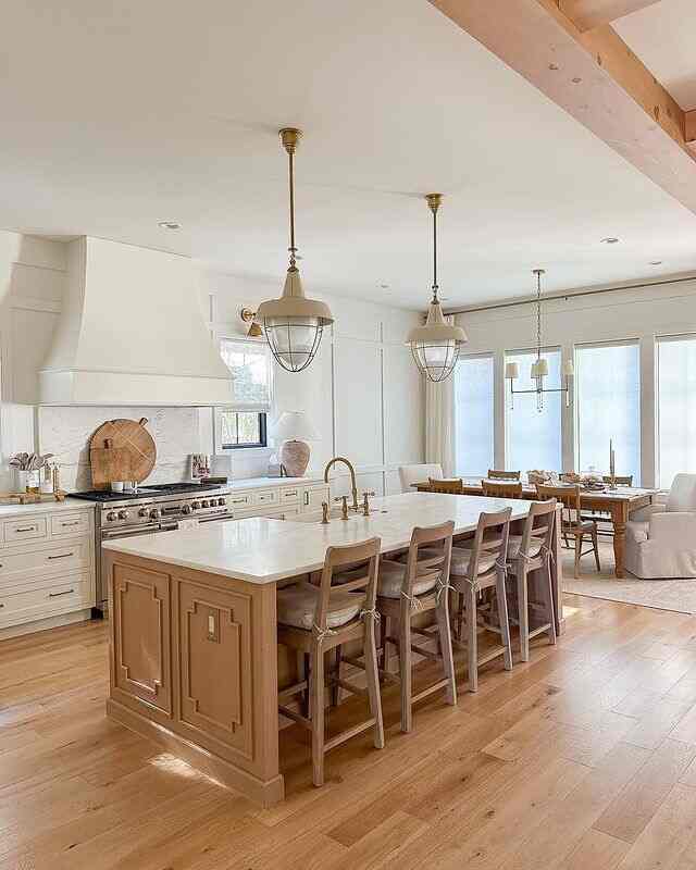 A bright open kitchen and dining room featuring white cabinetry and wood tones with a natural, elegant atmosphere