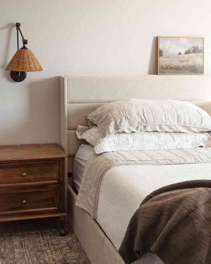 Natural color toned bedroom featuring beige bed, brown nightstand, and rattan wall lamp in a simple cozy setting