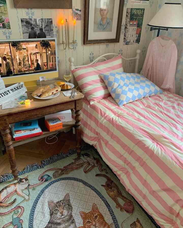 Bedroom with pink and white striped bedding, cat-patterned rug and wooden table creating a cozy atmosphere