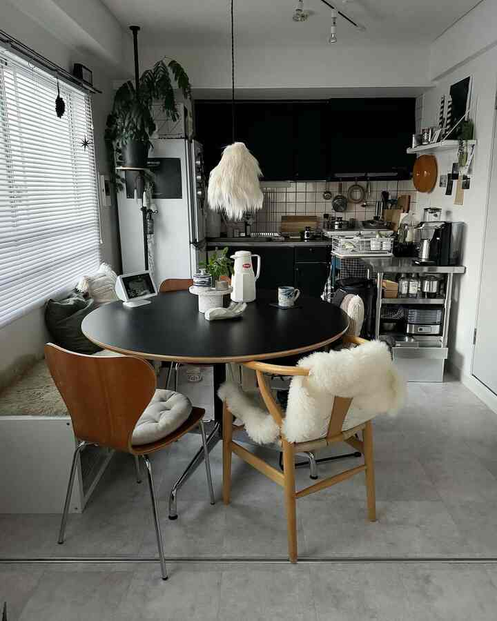 Modern kitchen and dining room in compact space featuring black cabinetry and wood tone chairs with a clean, minimal aesthetic