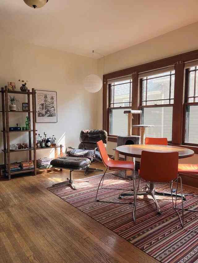Mid-Century Modern living room featuring warm wood tones, orange dining chairs, a comfortable armchair, and a striped rug with natural light