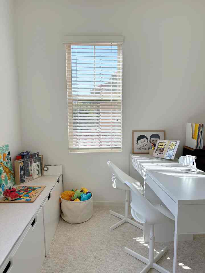 A bright and cozy kids' room in white and natural tones, featuring a desk and toy storage bench under sunlight