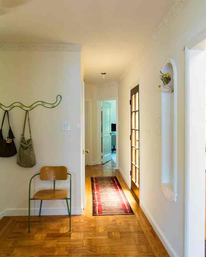White tone walls and ceiling with natural wood floor featuring a red rug and wooden chair in a long narrow entrance hallway