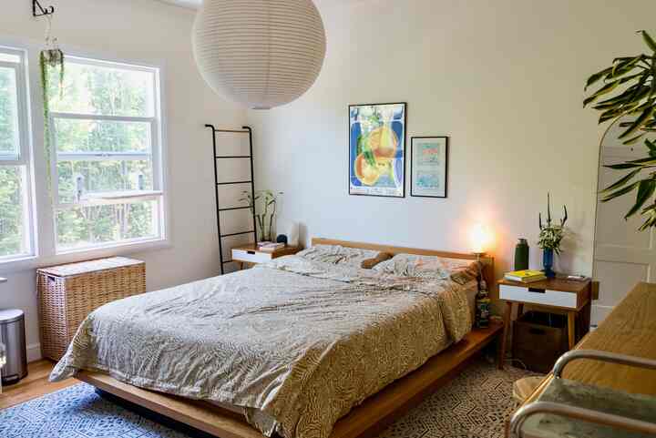 White-walled bedroom with natural wood tone furniture, featuring nightstands and a large paper pendant light in a minimalist setting