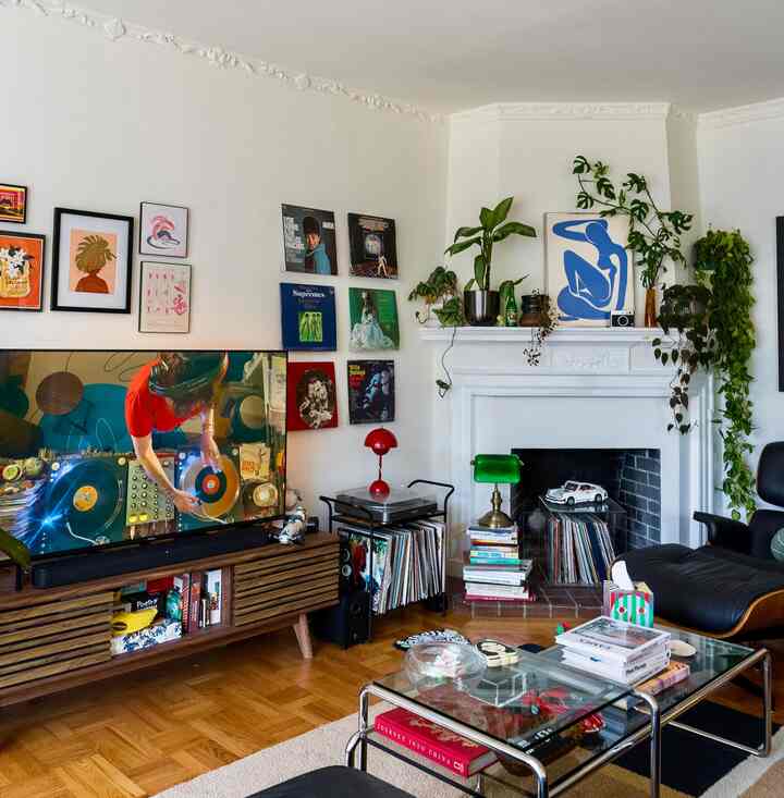 Living room with white walls and brown wooden floor, featuring an Eames lounge chair and ottoman, plants, and mid-century modern style elements