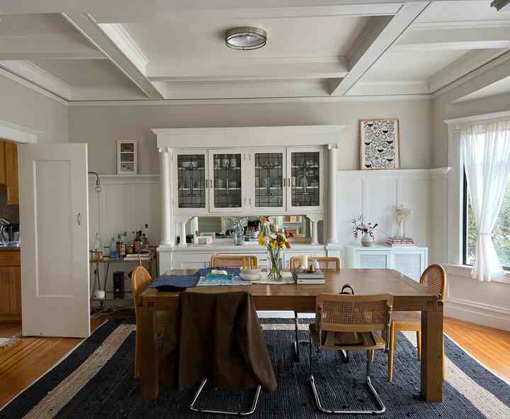 Natural wood-toned dining room featuring vintage cabinet with stained glass and flower vases, creating a cozy home party atmosphere